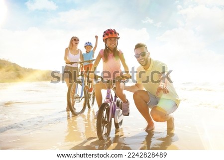 Happy parents teaching children to ride bicycles near sea on sunny day