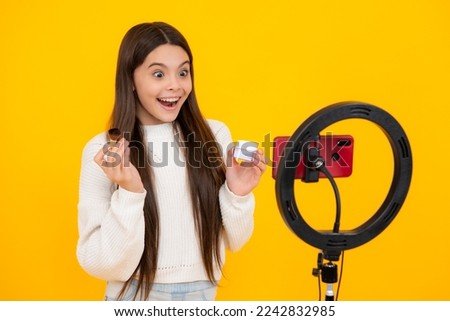 Teen girl speaking in front of camera for vlog isolated on yellow background. Teenager working as blogger, recording video blog. Excited face. Beauty blog, presenting makeup cosmetics powder brush.