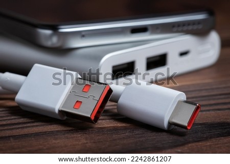 Portable power bank with USB cable and smartphone for charging mobile devices.