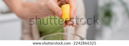 Cropped view of woman squeezing lemon above blender in kitchen, banner