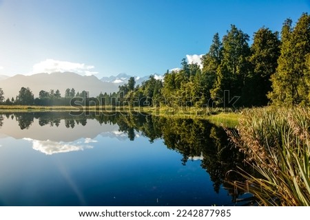 Reflections in Lake Mathieson surrounded by natural bush and forest and Southern Alps mountain range in South Island New Zealand. Royalty-Free Stock Photo #2242877985