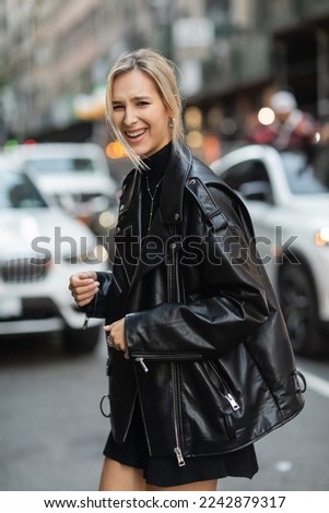 portrait of blonde woman in stylish leather jacket laughing on urban street in New York