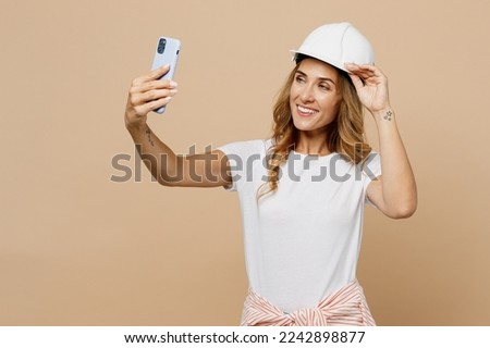 Young employee laborer handyman woman in white t-shirt helmet do selfie shot on mobile cell phone isolated on plain beige background Instruments accessories for renovation room. Repair home concept