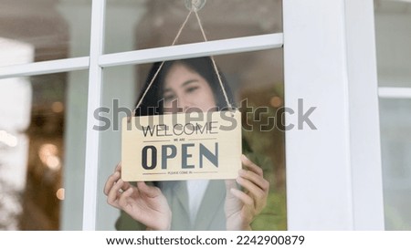 Woman store owner turning open sign broad through the door glass and ready to service. Small business woman owner turning the sign for the reopening	