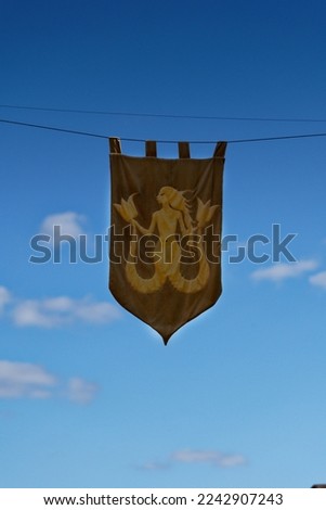 Mermaid coat of arms on fabric hanging with a blue sky during a medieval festival in Monpazier, a small village in Dordogne 