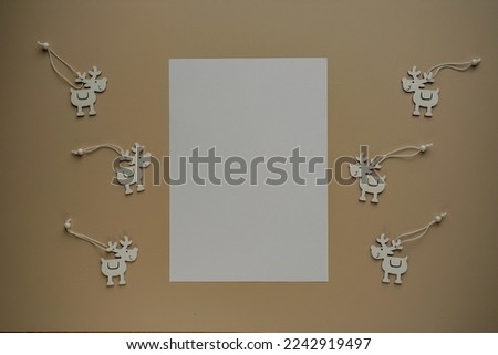 Blank sheets of paper with copy space for text and deers made of wood close-up view from above DIY on beige background. Children paper crafts, New Year Christmas decor. Blurred background