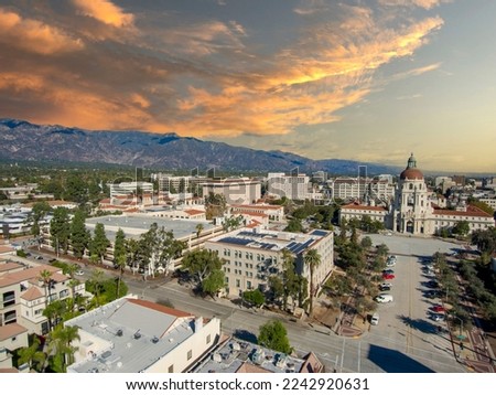 aerial shot of office buildings, city hall and apartments in the city skyline surrounded by lush green trees and plants, cars on the street, mountains and powerful clouds at sunset in Pasadena Royalty-Free Stock Photo #2242920631