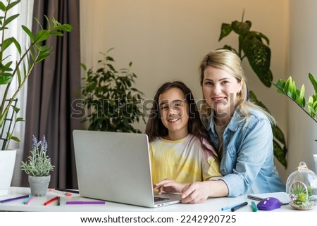 Beautiful mother and child looks at laptop screen spend time in kitchen using app education program, choose cartoons, teach kid pc usage, controls what daughter watching on internet cyberspace concept