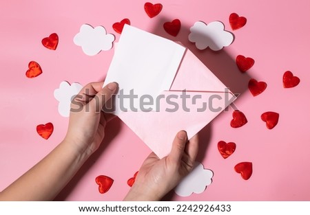 Hand holding a blank letter form for Valentine's Day or Mother's Day over an envelope with hearts. Mockup