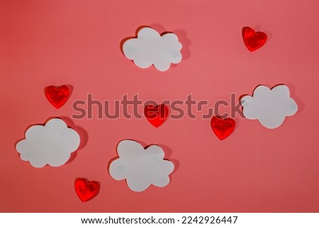 White paper clouds and red textile hearts on a red background. Conceptual background for Valentine's Day or Women's Day. Copy space.