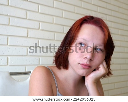 portrait of a pensive red-haired teenage girl against a brick wall.