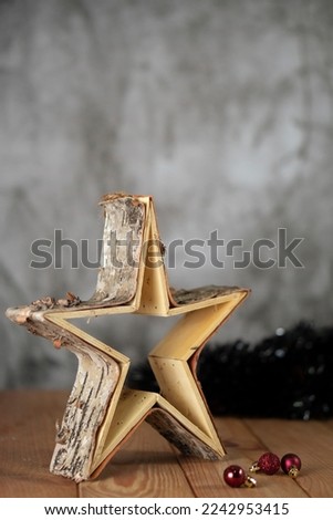 Wooden christmas star decoration standing on a wooden table, with black tinsel on the back, red christmas tree balls and and a grey background.	