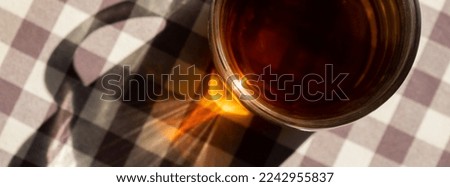 Cup of black tea with sunbeams and shadows. Healthy homemade tea in glass cup on table. Herbal medicine Delicious tea. Green clearing