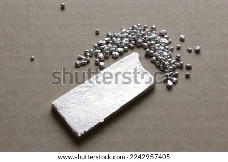 Precious metal smelted into a silver ingot, grains of 925 sterling silver 925 nearby. An essential foor jewelry making, and a reference on financial market. Royalty-Free Stock Photo #2242957405