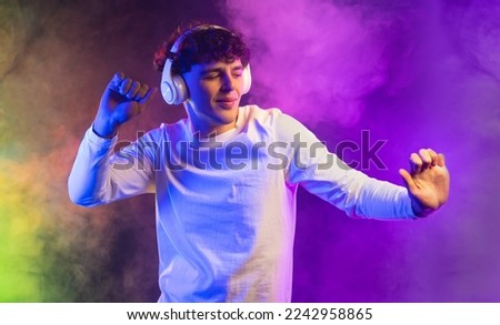 Positive man listening music with headphones, dancing on dark neon background. Stylish student guy enjoying life, active energy, inspired dance concept. High quality photo
