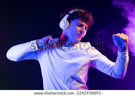 Positive man listening music with headphones, dancing on dark neon background. Stylish student guy enjoying life, active energy, inspired dance concept. High quality photo
