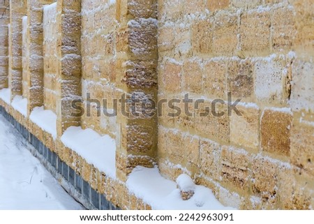 High stone fence made with the shell rock blocks partly covered with fluffy snow in overcast weather
