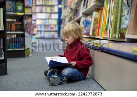 Cute blond toddler child, boy, reading book in a book store, wintertime