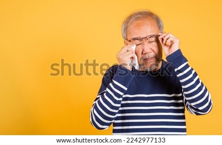 Portrait Asian senior old man sad wiping away his tears studio shot isolated on yellow background, Elder man crying raise glasses with tissue wipe red eyes, Sadness depressed lonely Royalty-Free Stock Photo #2242977133