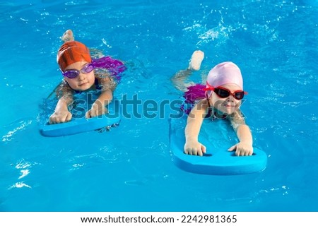 Two little girls having fun in pool learning how to swim using flutter boards Royalty-Free Stock Photo #2242981365