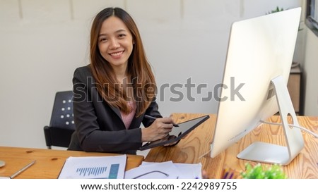 Asian businesswoman holding a file folder, smiling, and looking away outside while standing in an office room.