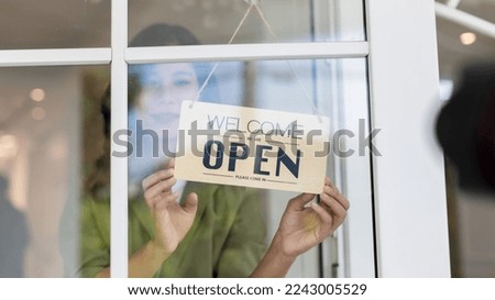 Woman store owner turning open sign broad through the door glass and ready to service. Small business woman owner turning the sign for the reopening	