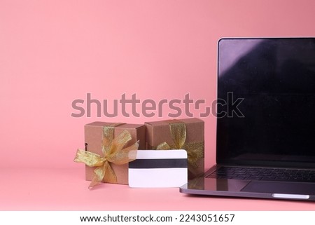 Black Friday concept. Cropped of blank screen laptop, gift box with gold ribbon and credit card isolated on pink background. 