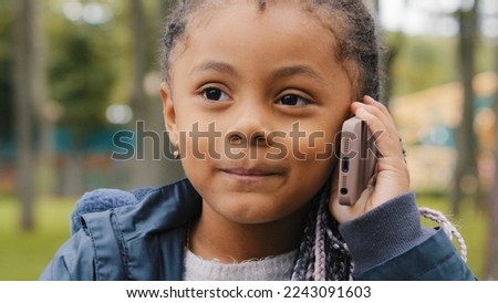 Little ethnic girl talking on mobile phone outdoors portrait funny multiracial child answer telephone call small African American baby kid daughter schoolgirl standing in street talk with smartphone