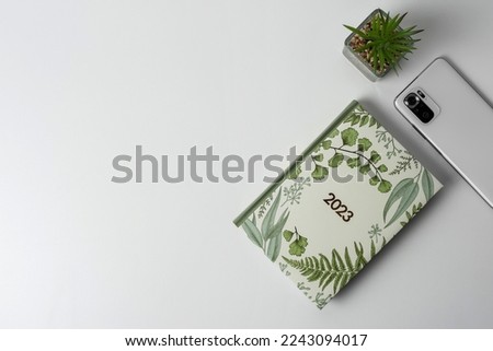 A notebook, a plant and a smartphone on a light background. Top view. Copy space.