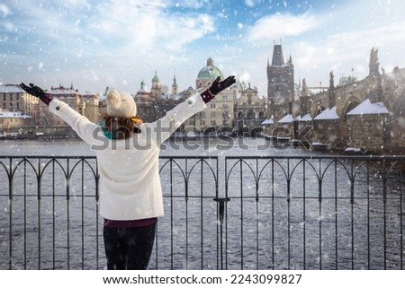A happy tourist woman in winter clothing enjoys the view of the skyline of Prague with Charles Bridge and old town with snow 