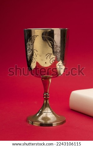 beautiful golden chalice on light beige bible with red background Royalty-Free Stock Photo #2243106115