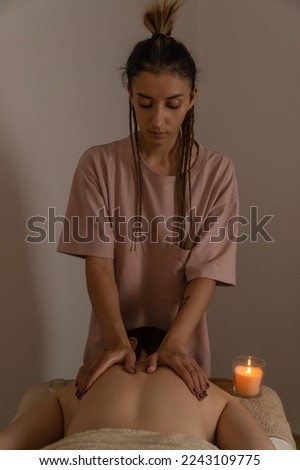 Masseur does a back massage standing at the head of a woman lying on a massage couch in a warm atmosphere. Concept of spa, health. Vertical photo