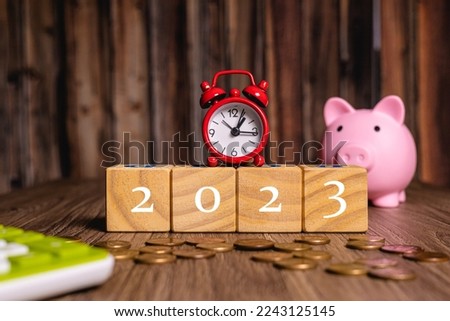The year 2023 on wooden cubes with a piggy bank, a calculator and a clock in the composition. Economy and finance.

