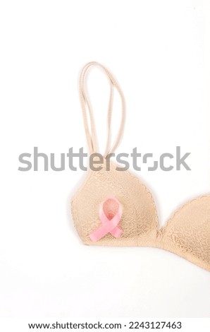 Pink ribbon attached over to beige brassiere on white background. Breast cancer concept. Copy space. 