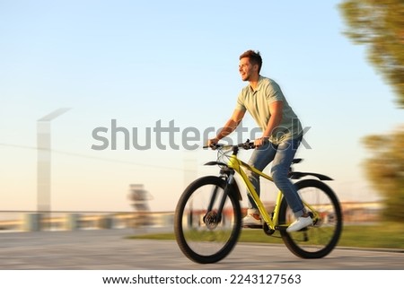 Handsome young man riding bicycle on city waterfront, motion blur effect