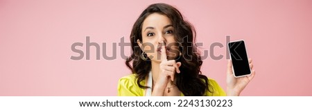 brunette housewife holding smartphone with blank screen and showing hush sign isolated on pink, banner