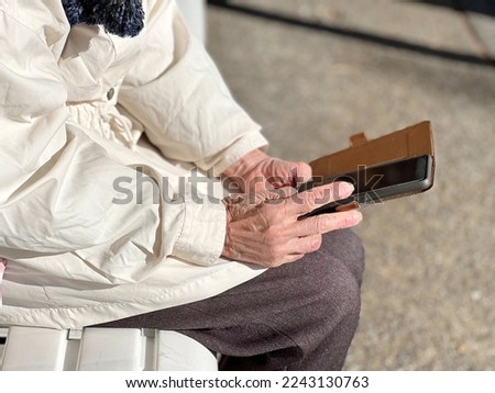 Close-up of an elderly woman's hand sitting on a bench and operating a smartphone Royalty-Free Stock Photo #2243130763