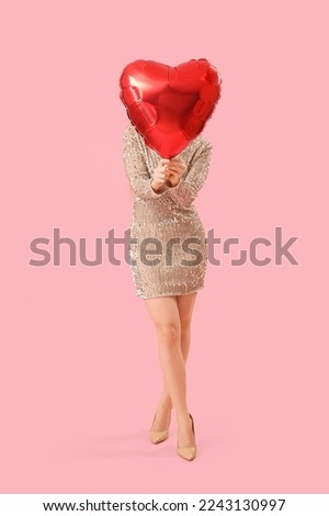 Young woman hiding face behind heart-shaped balloon on pink background. Valentine's Day celebration
