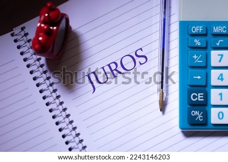 The word interest in Brazilian Portuguese written on a notebook sheet with a pen, a clock and a calculator in the composition. Brazilian economy and finance.
