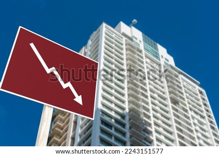 A sign showing an downward arrow in front of a highrise condominium or apartment. Concept of decreasing or slumping condo prices and value or a real estate bust. Royalty-Free Stock Photo #2243151577