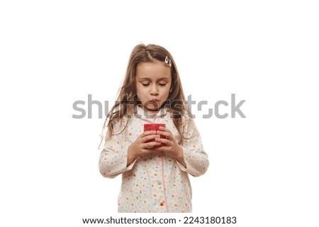 Adorable Caucasian child, a lovely little girl with beautiful long hair, in soft pajamas, blowing out a red candle before going to bed, isolated on white background. Copy space
