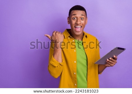 Photo portrait of attractive young male excited point empty space hold gadget wear trendy yellow outfit isolated on purple color background