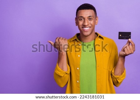 Photo portrait of handsome young man hold credit bank client point empty space wear trendy yellow look isolated on purple color background