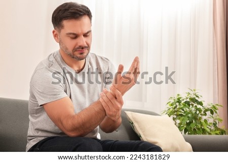 Man suffering from pain in his hand on sofa indoors Royalty-Free Stock Photo #2243181829