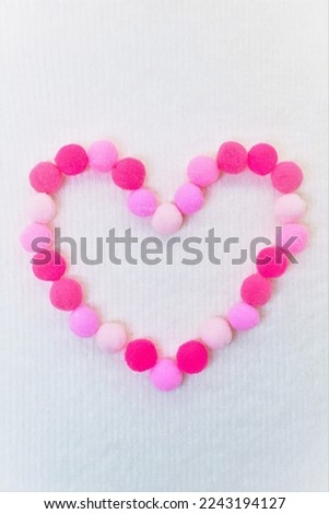 Large heart shape made of pinkish pompons on a fluffy fabric white background, vertical