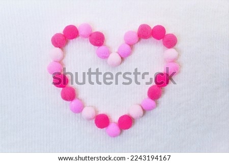 A big heart mark made of pink pompoms on a white background of soft winter fabric