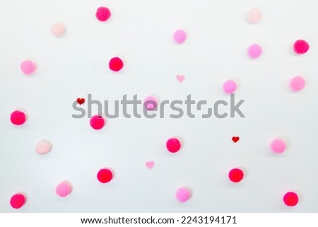 Polka dots with red and pink pompoms and small hearts scattered on a soft white fabric background