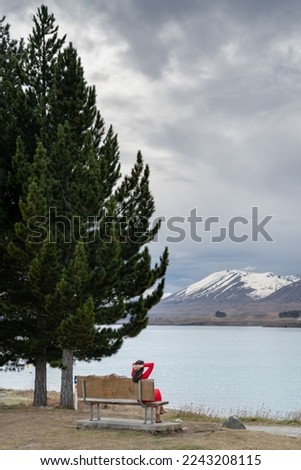Asian female tourist pose at turquoise color Lake Tekapo with snow capped New Zealand southern alps at the background. Best travel destination in New Zealand. 