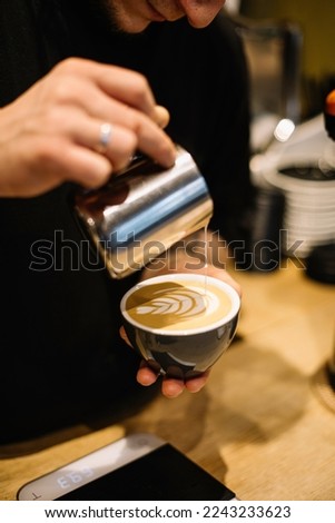 Young male barista pouring frothed milk into the cup with freshly brewed double espresso coffee, making latte art, close up vertical view Royalty-Free Stock Photo #2243233623