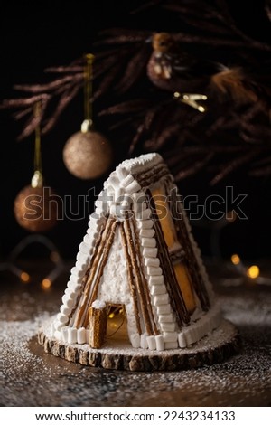 Handmade gingerbread A-form house for Christmas and New Year with icing sugar snow on a dark background with decorations and Christmas lights.